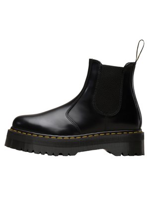 Botte Chelsea en cuir noir avec panneau latéral élastique, semelle épaisse striée, couture jaune et languette de traction au talon.