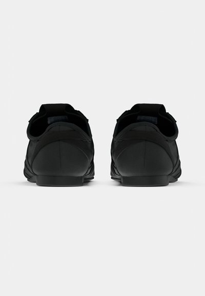 Μαύρα αθλητικά παπούτσια με λείο υφασμάτινο εξωτερικό, χαμηλό προφίλ, μαξιλαρωμένη φτέρνα και μινιμαλιστική αισ θητική χωρίς εμφανή λογότυπα.