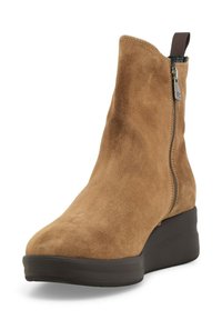 Stivale alla caviglia in suede marrone con punta arrotondata, chiusura con zip e suola a zeppa. Presenta una tomaia testurizzata e un nasello in tessuto per un facile indossamento.