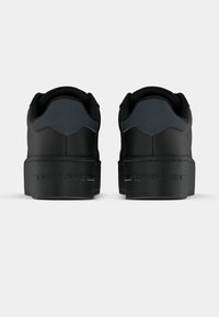 Černé tenisky s hladkým matným povrchem, s polstrovaným límcem, tlustou podrážkou a vyraženým nápisem "TOMMY JEANS" na patě.