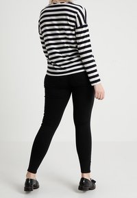 Randig långärmad topp i marinblått och krämfärgat, kombinerad med svarta skinny jeans. Toppens passform är bekväm och ytfinishen är slät. Svarta skor fulländar stilen.