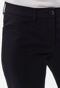Svarta byxor med en slät tygstruktur, med en framficka, knappstängning och passpoaler. Minimalistisk design med platta sömmar.