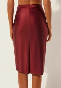 Bleistiftrock aus burgunderrotem Satin, knielang mit einer glatten Textur, hinten mit Schlitz und dezentem Raffdetail an der Taille.