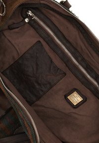 Interno in tessuto e pelle marrone di una borsa che presenta una tasca con cerniera, una patch in pelle marrone e dettagli in tessuto a righe lungo il bordo.