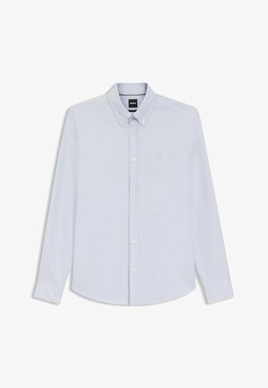 Chemise bleu clair à manches longues avec un col boutonné, des boutons blancs et un logo brodé discret sur la poitrine. Texture de tissu lisse.