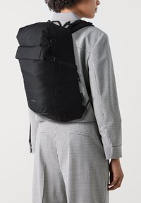 Zaino nero con spallacci regolabili e tasca frontale, caratterizzato da un design elegante e rettangolare e da una texture del tessuto resistente.