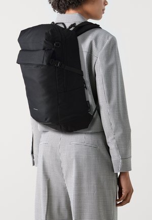Černý batoh s nastavitelnými popruhy a přední kapsou, vyznačující se elegantním obdélníkovým designem a odolnou texturou látky.