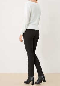 Pull blanc avec manches longues plissées, associé à un pantalon noir ajusté et des bottines à talons. Lignes épurées et design minimaliste.