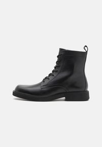 Bottines en cuir noir avec bout rond, lacets à l'avant et surface texturée. Comprend une languette à l'arrière et une semelle en caoutchouc solide pour une meilleure adhérence.
