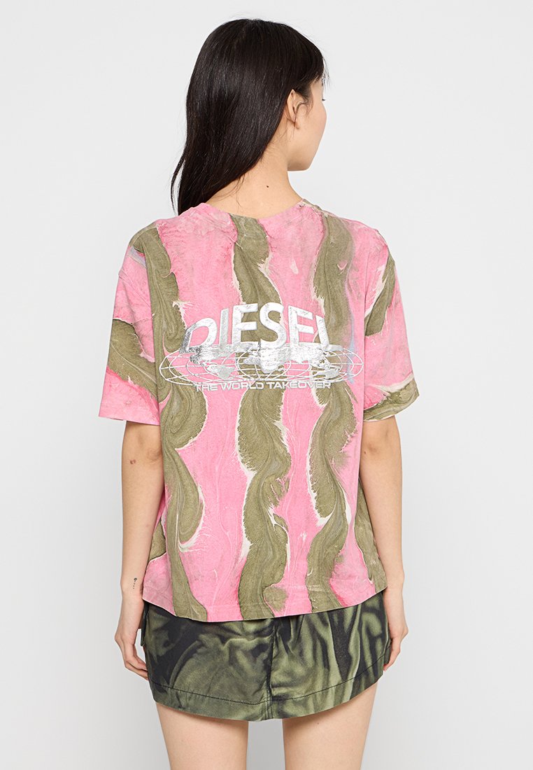 T-shirt rosa con swirl verdi astratti, vestibilità ampia, e logo metallico argento "DIESEL" con testo, indossato sopra pantaloni corti verde scuro.