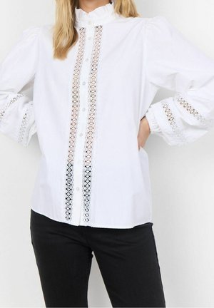 Weiße Bluse mit Spitzenapplikationen entlang der Vorderseite und Ärmel. Sie hat einen hohen Kragen und Knöpfe. Das Baumwollmaterial sorgt für eine glatte Textur.