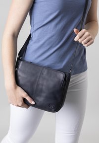 Black leather crossbody bag with a smooth texture, featuring a zippered compartment and an adjustable strap, worn casually.