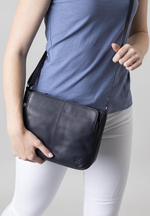 Black leather crossbody bag with a smooth texture, featuring a zippered compartment and an adjustable strap, worn casually.