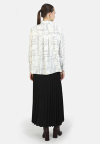 Camicia bianca con linee geometriche nere, maniche lunghe e colletto a punta, abbinata a una gonna plissettata nera e stivali con tacco.