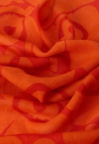 Πορτοκαλί ύφασμα με υφή που διαθέτει ένα διακριτικό μοτίβο σε σκουρότερο κόκκινο τόνο, παρουσιάζοντας απαλή ρέουσα πτώση και πτυχώσεις.