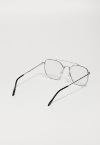 Gafas de metal con un marco plateado, lentes cuadrados y puntas de plástico negro en las patillas. Diseño ligero con un hardware mínimo.