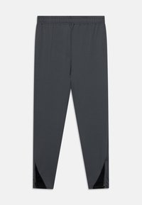 Grå treningsbukser med elastisk linning, tapered design og glidelåsdetaljer på de nedre sidene. Laget av lett, glatt stoff.
