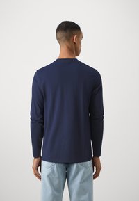 Langarm T-shirt van marineblauwe katoen met een ronde hals, met een gladde textuur en een relaxte pasvorm, gedragen met lichtblauwe jeans.