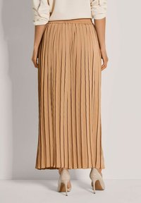 Plisse midi rok in licht bruin, met een elastische tailleband. Zachte textuur met verticale plooien, gecombineerd met beige hoge hakken.
