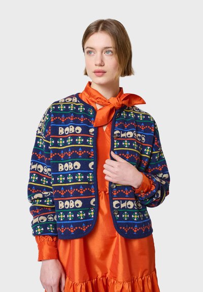 Cárdigan navy con patrones geométricos multicolores y texto, con un cuello redondo y botones. Se lleva sobre un vestido naranja.