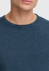 Granatowy sweter z prążkowanego dzianiny z okrągłym dekoltem, o teksturowanej powierzchni i dopasowanym kroju. Zbliżenie na dekolt i materiał.