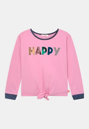 Chemise rose à manches longues avec poignets et encolure foncés, un nœud devant à l'ourlet, et le mot "HAPPY" en lettres multicolores sur la poitrine.
