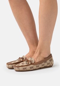 Mocassins marron et beige avec un motif texturé, présentant un détail en nœud, des bords en cuir et des accents de logo sur les côtés.
