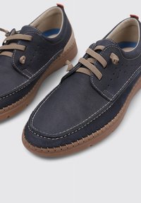 Zapatos de cuero marino con acentos beiges, diseño de cordones, lados perforados, suela en contraste color marrón claro y detalle de costura visible.