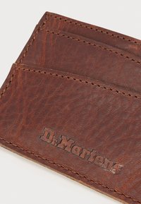 Καφέ δερμάτινη θήκη για κάρτες με υφασματική επιφάνεια, που διαθέτει πολλαπλές θέσεις για κάρτες και ανάγλυφο λογότυπο "Dr. Martens".