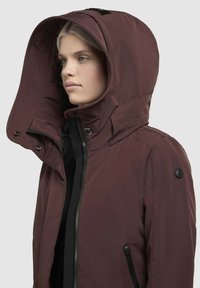 Bordo kapuce ar rāvējslēdzēju, matēta tekstūra un liela kapuce. Ar melniem akcentiem un pogu detaļām ap kaklu un piedurknēm.