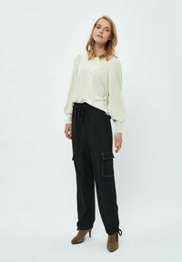 Top bianco a maniche lunghe con spalle a sbuffo, abbinato a pantaloni cargo neri con tasca laterale e polsini regolabili. Stivali con tacco marroni.