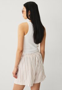 Top blanco sin mangas y pantalones cortos a rayas beige. Los pantalones cortos tienen una cinturilla elástica y un corte relajado, compuestos de una tela ligera.