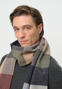 Écharpe en laine présentant un motif à carreaux multicolore dans les tons de gris, marine, beige et bordeaux, mettant en valeur une texture douce et un design chaleureux.