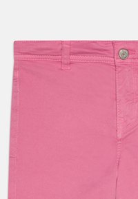 Jeans en denim rose avec une coupe droite, un design à cinq poches et un bouton supérieur. Coutures visibles le long des coutures et de la taille.