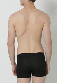 Zwarte katoenen boxershort met een zachte tailleband, voorzien van een comfortabele pasvorm en zachte textuur, weergegeven van achteren tegen een neutrale achtergrond.