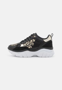 Sneaker nera con motivi floreali dorati, pannelli in rete e camoscio, suola spessa bianca, lacci sulla parte frontale e linguetta sul tallone, su sfondo bianco.