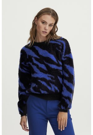 Sort fuzzy sweater med blå zebra-striber, har en rund halsudskæring og lange ærmer. Stylet med blå bukser.