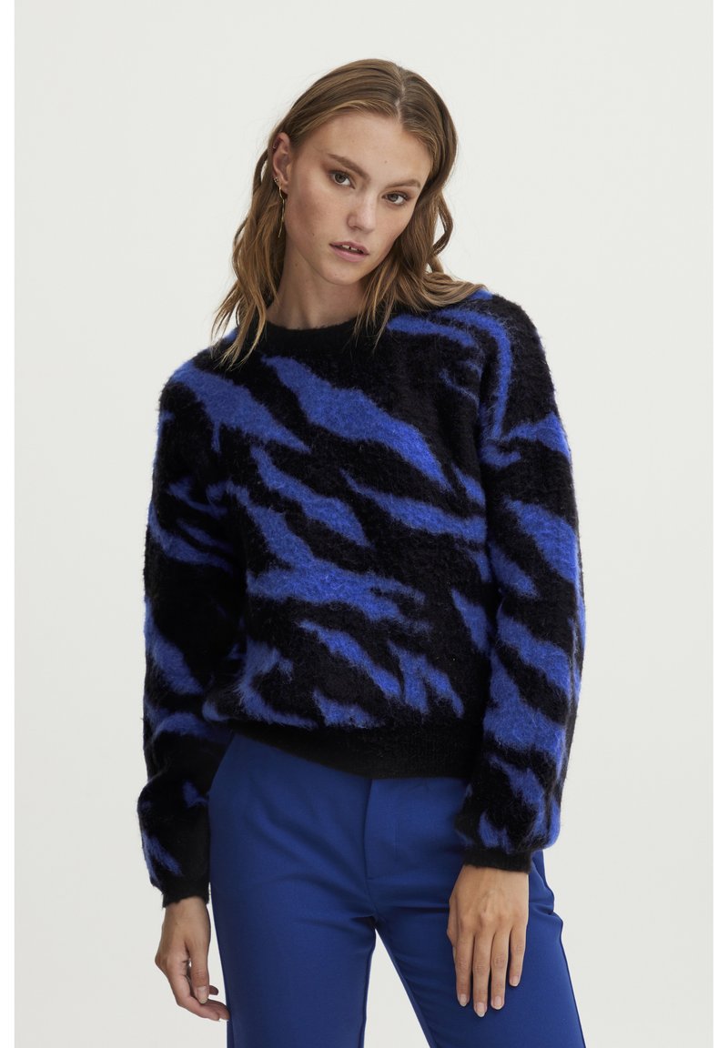 Črn puhast pulover z modrimi zebrski črtami, ima okroglo ovratnico in dolge rokave. Uslužen z modrimi hlačami.