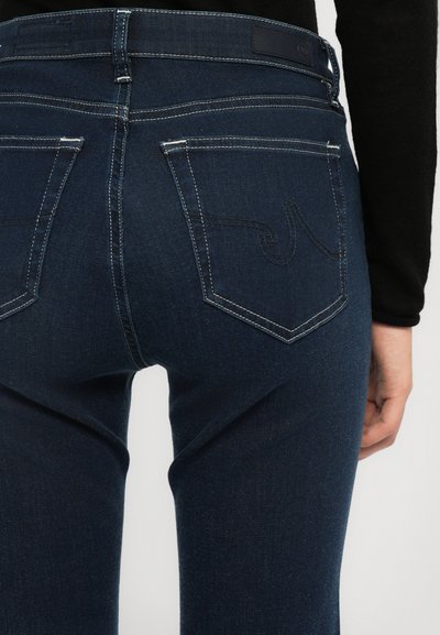 Jeans de mezclilla azul oscuro con una cintura de altura media, bolsillos traseros con detalles de costura y un ligero desvanecimiento a lo largo de las piernas.