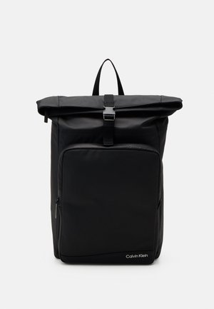 Sac à dos noir à fermeture roulante avec poche zippée à l'avant, boucle supérieure, poignée de transport et logo Calvin Klein en bas à droite.