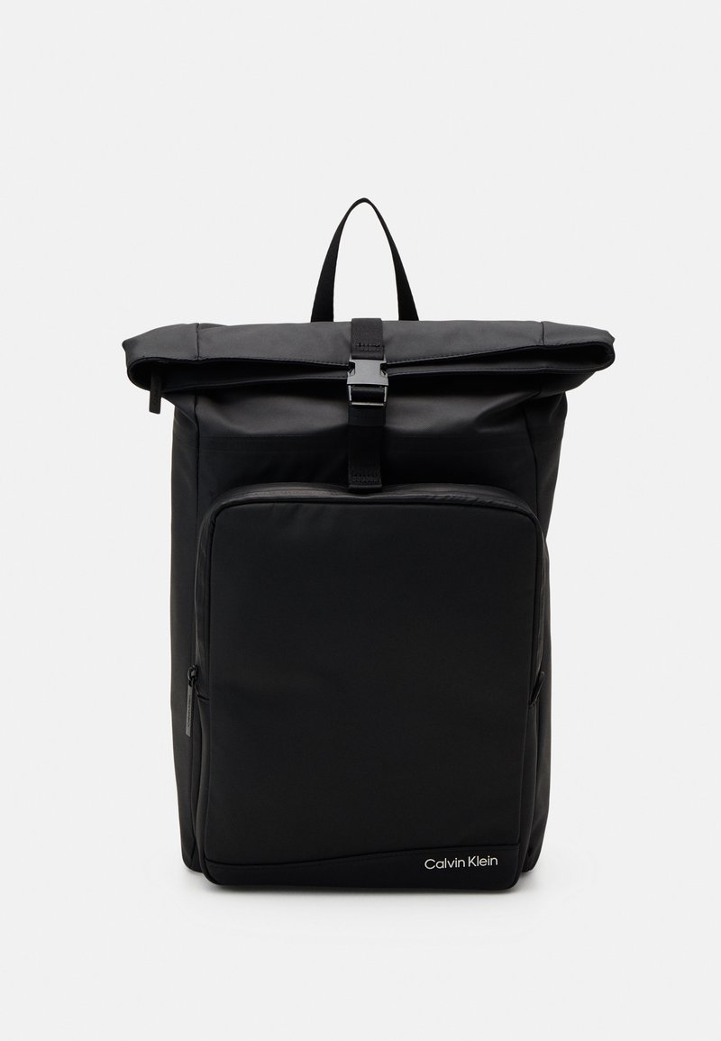 Sac à dos noir à fermeture roulante avec poche zippée à l'avant, boucle supérieure, poignée de transport et logo Calvin Klein en bas à droite.