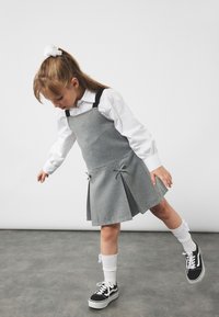 Harmaa neuletunika mustilla olkaimilla, laskostettu hame ja silkkinauhat yksityiskohtina. Valkoinen nappipaita ja mustat lenkkarit valkoisilla pohjilla täydentävät asun.