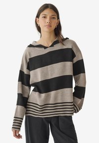 Sweat à capuche rayé en beige et noir, avec de larges rayures horizontales et un bord côtelé en bas de vêtement et aux poignets pour plus de texture.