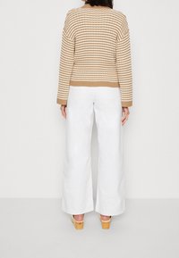 Gestreifter beiger und weißer Pullover mit geripptem Saum und Bündchen, kombiniert mit weißen weit geschnittenen Hosen und Holzsohlen-Clogs.