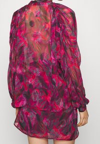 Blusa trasparente con motivo floreale in tonalità di rosa e rosso, con maniche a sbuffo e scollatura rotonda. Tessuto leggero con design fluido.