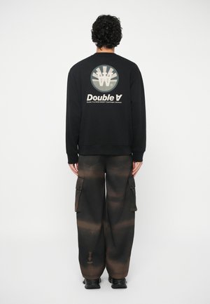 Sweatshirt preto com um gráfico circular e o texto "Double A" nas costas, combinado com calças cargo escuras com um padrão em degrade.
