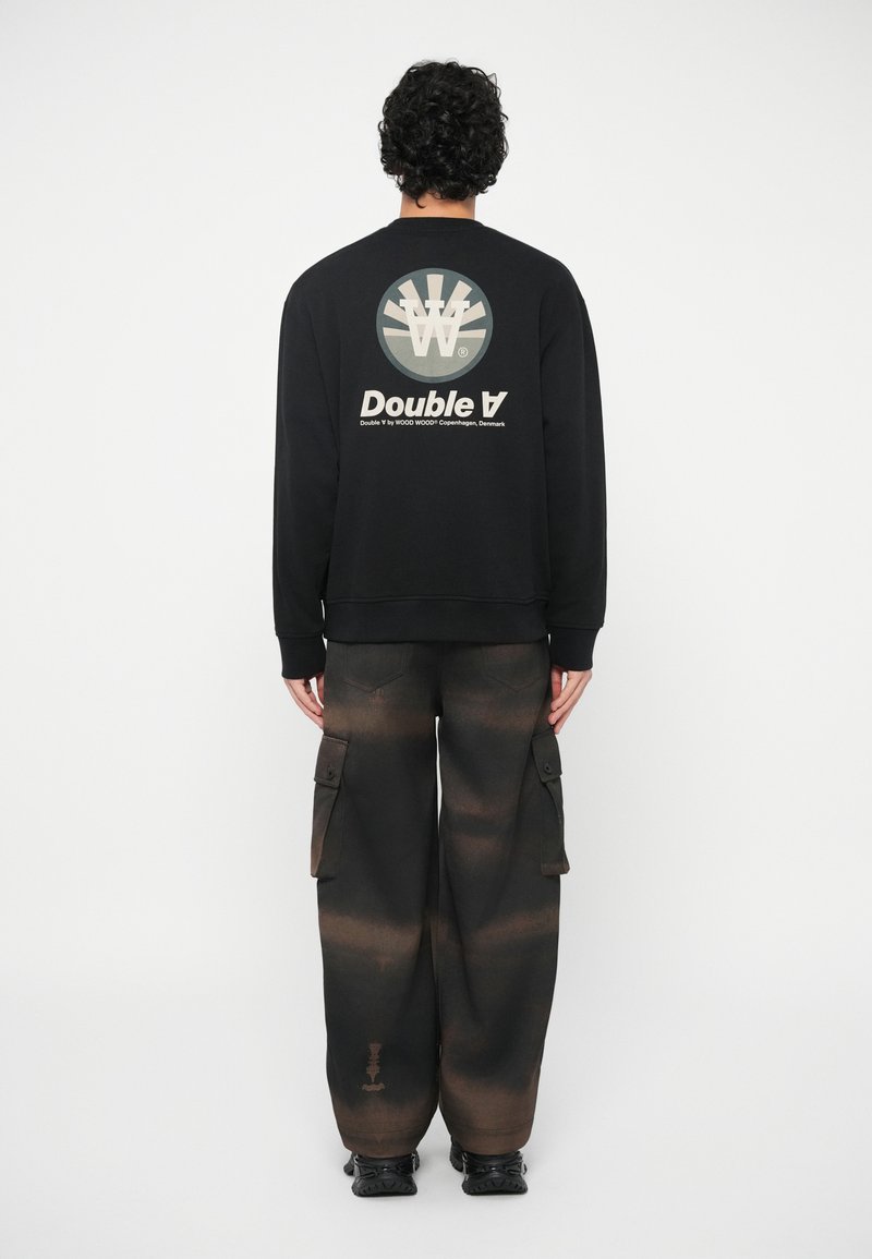 Μαύρη μπλούζα με κουκούλα με κυκλικό γραφικό και το κείμενο "Double A" στο πίσω μέρος, συνδυασμένη με σκούρες cargo παντελόνες που διαθέτουν gradient σχέδιο.