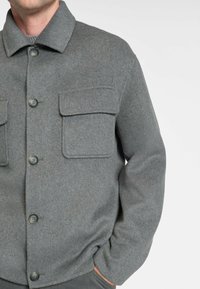 Grå uldjakke med krave, knaplukning foran, to brystlommer og lange ærmer. Har en blød tekstur og afslappet pasform.