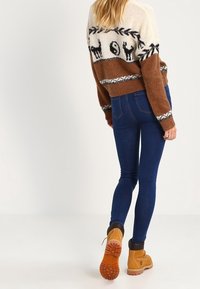 Knitted sweater with cotton-blend fabric, cream, brown, and black colors. Features animal designs and a pattern at the hem. Worn with blue jeans and boots.