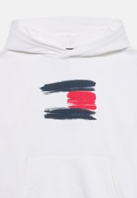 Vit hoodie med en framficka och en grafisk design av tre penseldrag-lika ränder i marinblå, röd och svart. Slät textur.